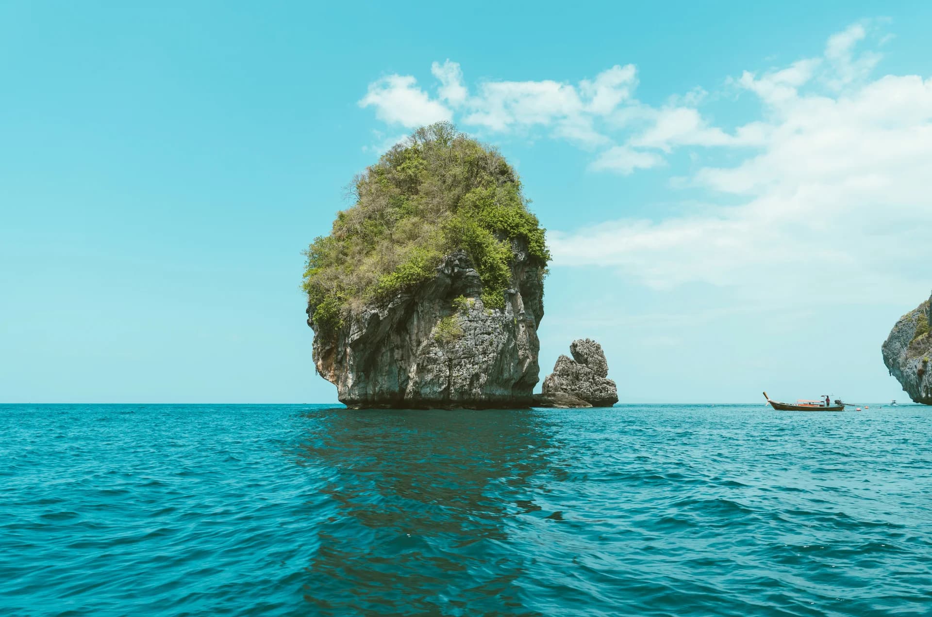 Isolotto roccioso ricoperto di vegetazione nel mare turchese della Thailandia con barca tradizionale