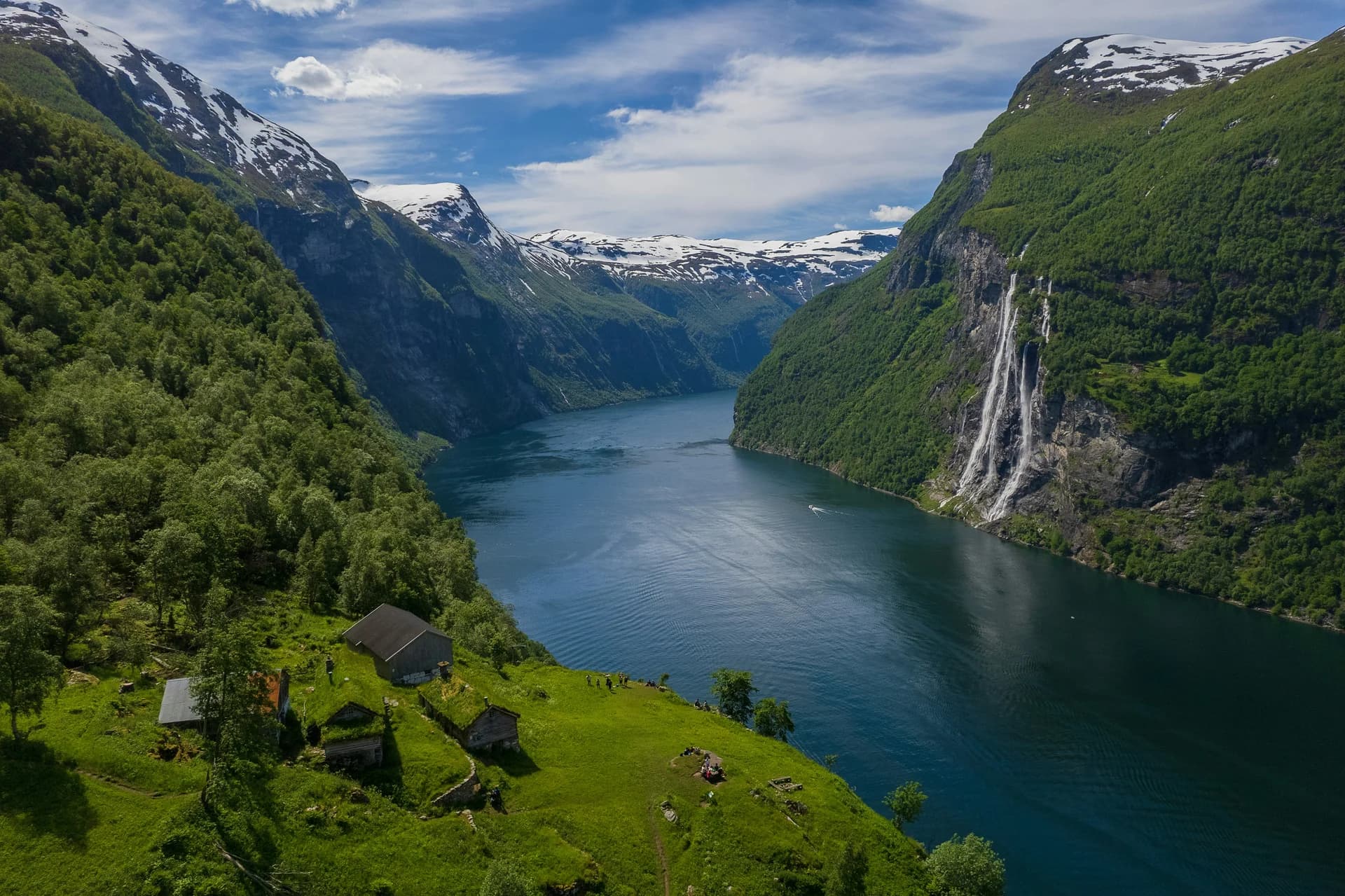 Il Geirangerfjord in Norvegia tra montagne verdi, una cascata e piccole casette tradizionali con tetto in erba
